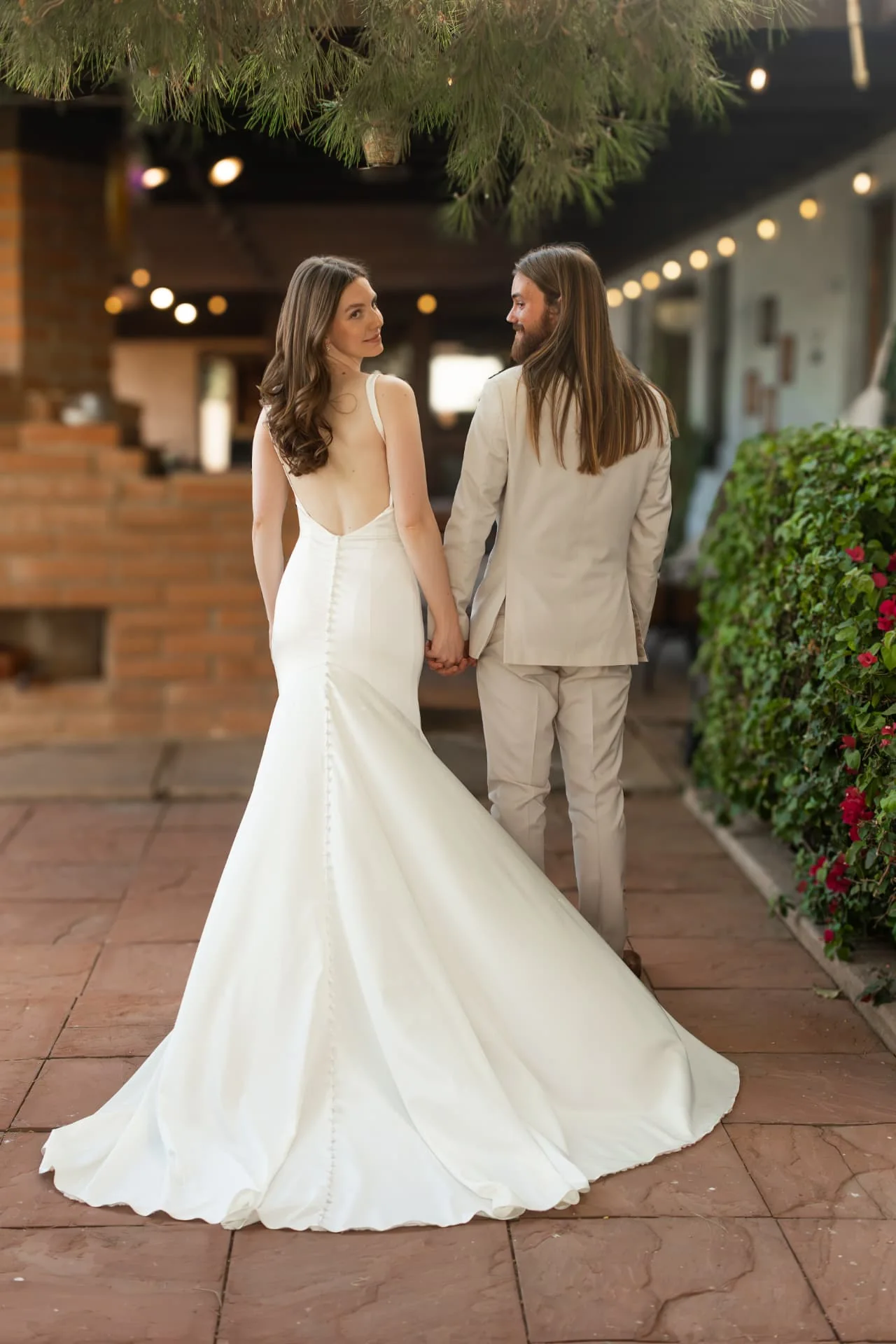 Bride and groom walking away hand in hand under string lights on a terracotta patio — romantic Scottsdale Arizona wedding