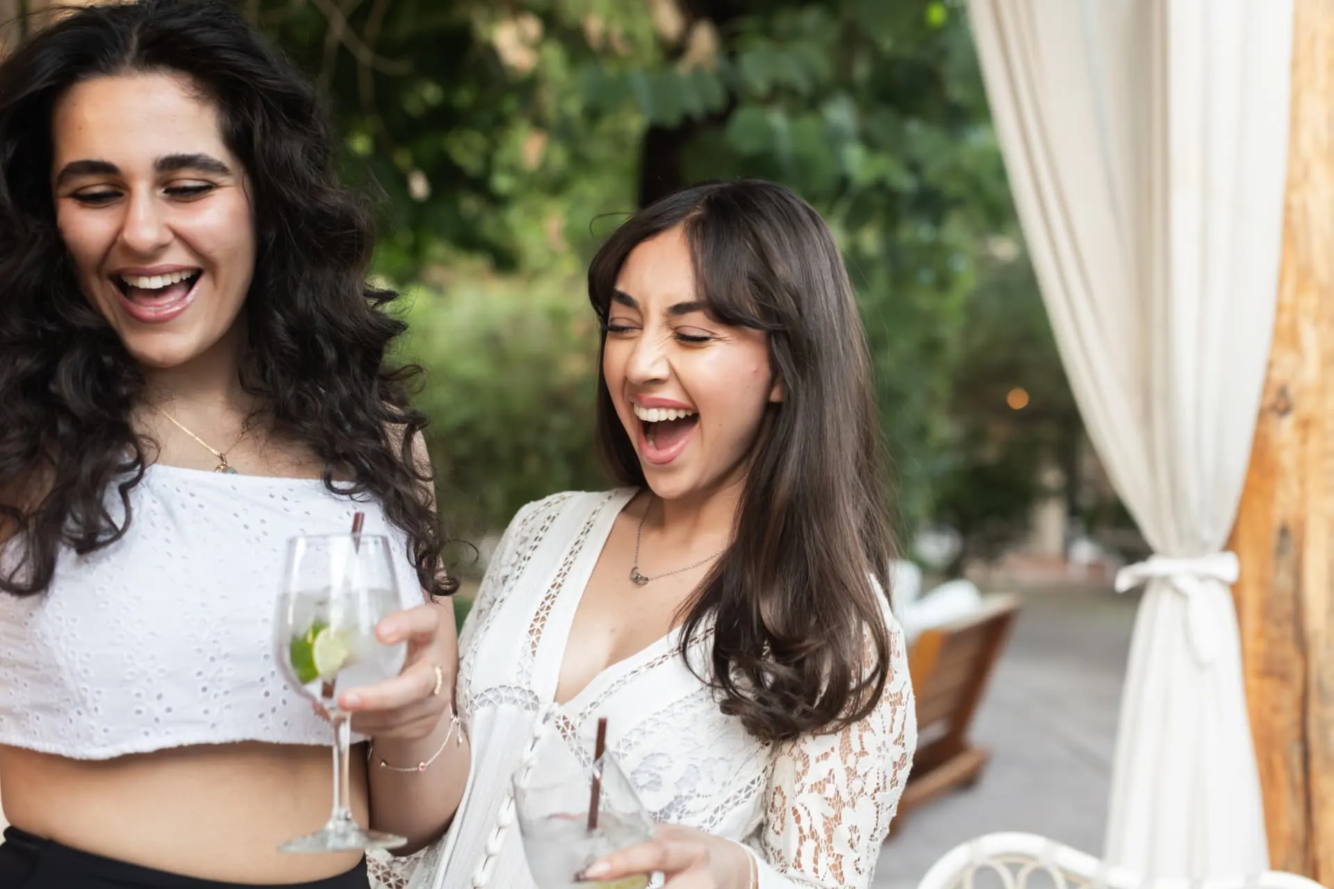 Two friends laughing with drinks at an Arizona bachelorette brunch