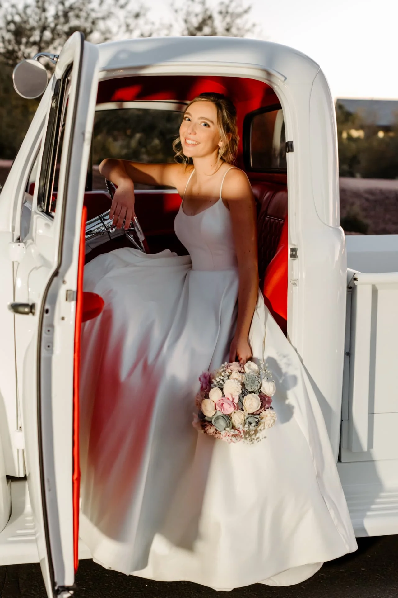 Bride in an ivory gown seated in the driver's seat of a white vintage truck with cherry-red leather interior at golden hour — Arizona wedding photography near Scottsdale