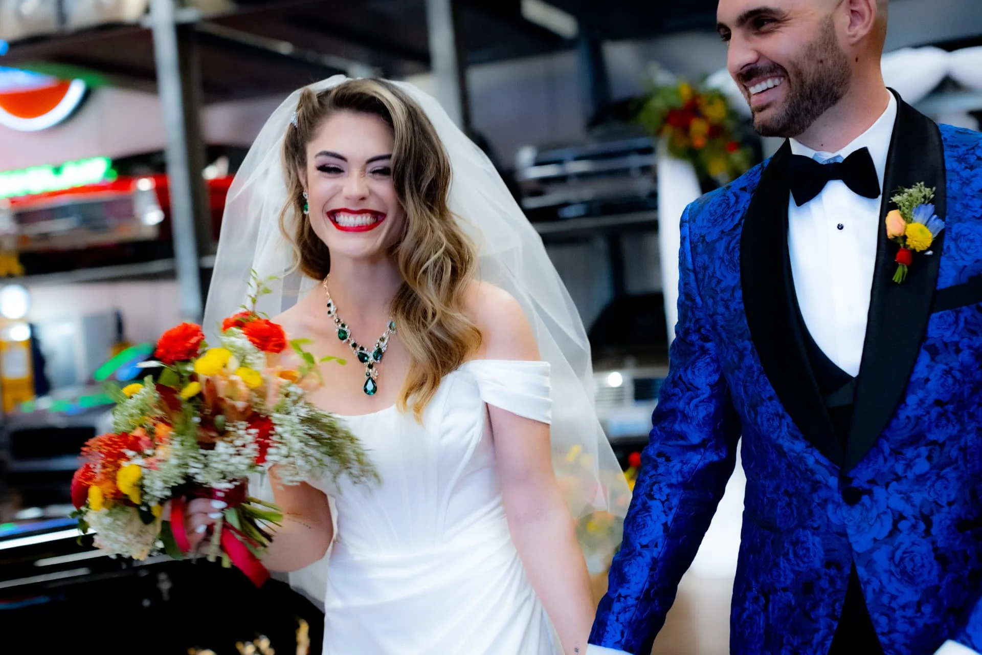 Laughing bride and groom walking hand in hand in front of classic cars on storage lifts — The Vault wedding in Scottsdale, Arizona